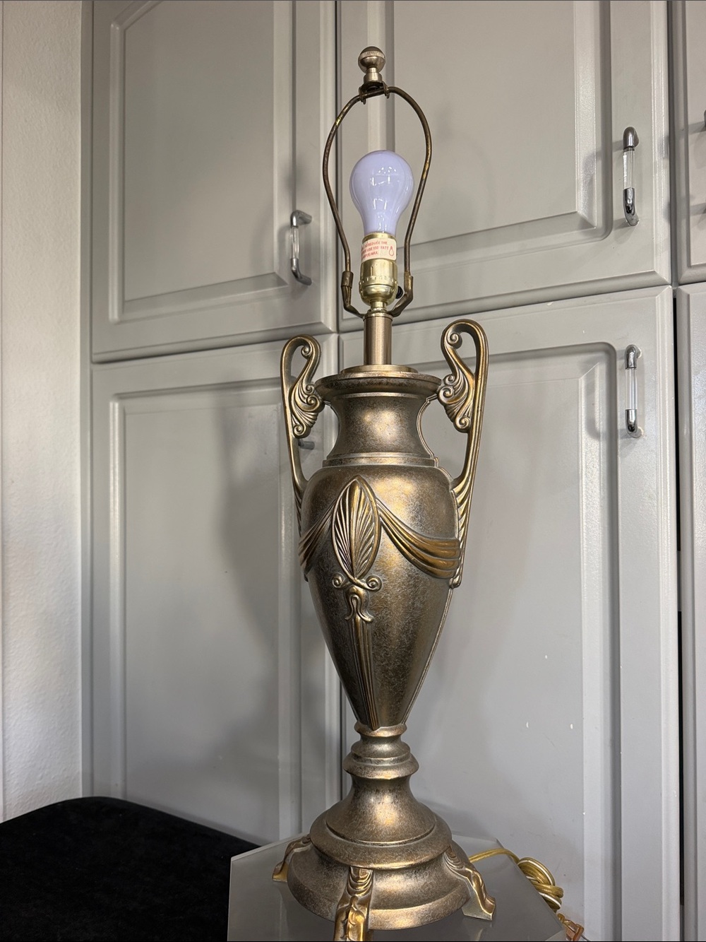 Vintage Grecian urn-style table lamp with ornate scroll handles, iron or metal.